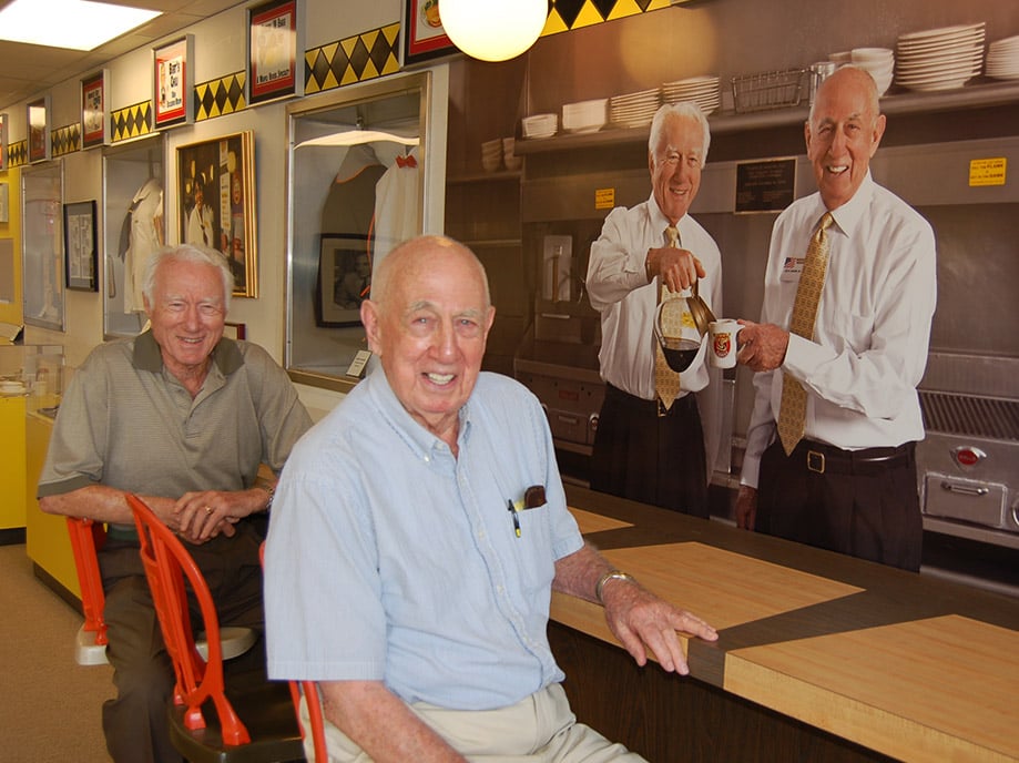 Joe Rogers Sr and Tom Forkner sitting in front of a print of their photo